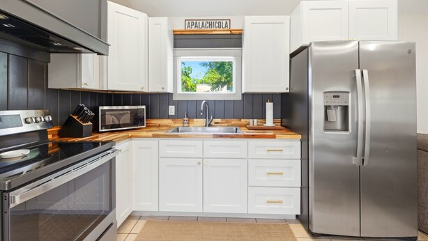 A modern kitchen with white cabinets, stainless steel appliances, a window, and a sign above the window. - Nautigull- A Fisherman's Delight (Apalachicola)