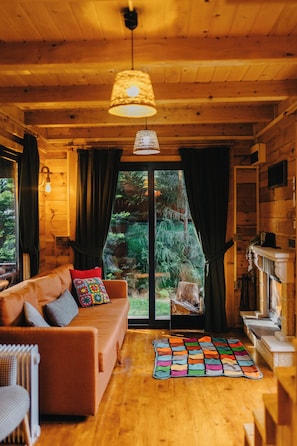 A cozy cabin interior with a wooden ceiling, a sofa with cushions, a colorful rug, and a fireplace. - Delmare Suit Villa (Ardeşen)