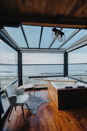 A modern interior with a wooden floor, a large window overlooking the sea, a seating area with chairs, and a hot tub. - Delmare Suit Villa (Ardeşen)