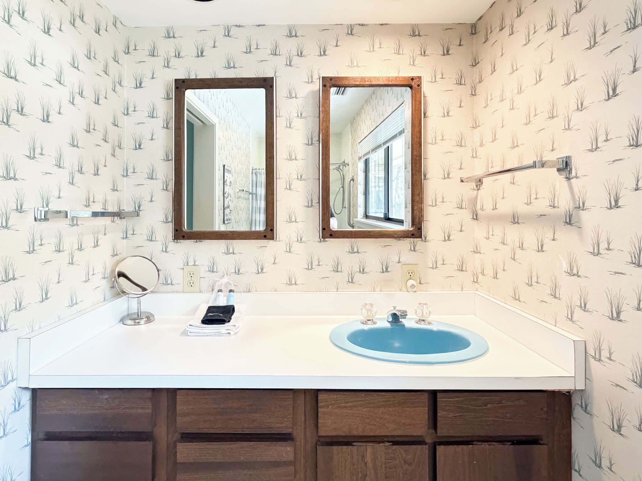 A bathroom with a white vanity, a blue sink, two mirrors, and a patterned wallpaper.