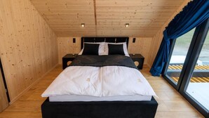 A wooden-paneled room with a bed, nightstands, and a window with curtains. - Comfortable Holiday Homes, Pool, Sauna, Jacuzzi (Darlowo)
