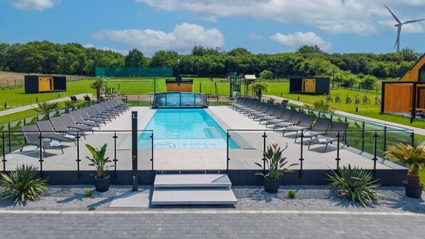 A swimming pool with sun loungers and a wind turbine in the background. - Comfortable Holiday Homes, Pool, Sauna, Jacuzzi (Darlowo)