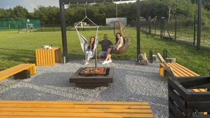 A hammock swing set, a fire pit, and wooden benches in an outdoor setting. - Comfortable Holiday Homes, Pool, Sauna, Jacuzzi (Darlowo)