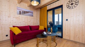 A room with wooden walls, a red sofa with yellow cushions, a round table with a gold base, and a large clock on the wall. - Comfortable Holiday Homes, Pool, Sauna, Jacuzzi (Darlowo)