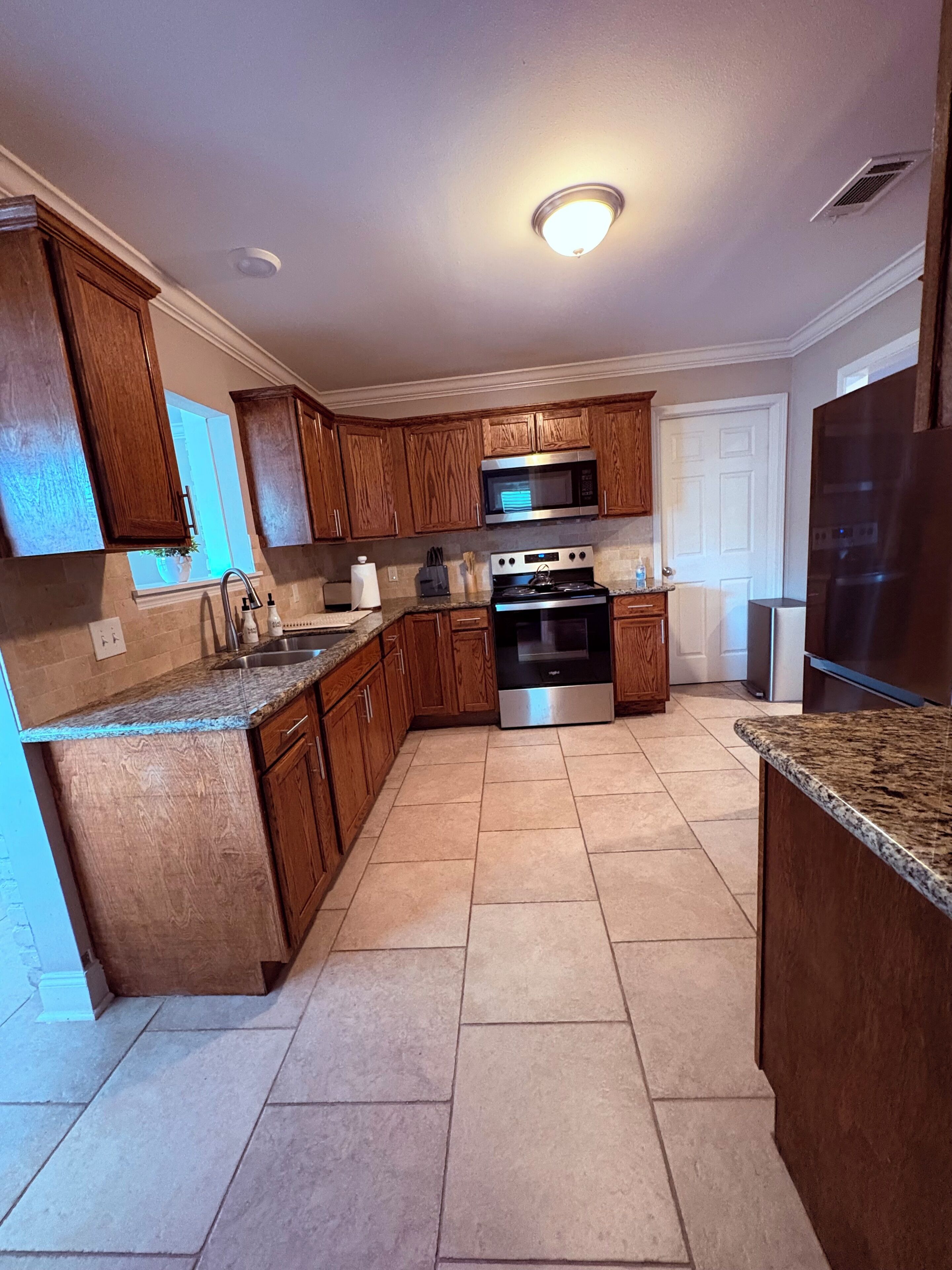 Una cocina con armarios de madera, microondas de acero inoxidable, horno, refrigerador y encimera de granito.