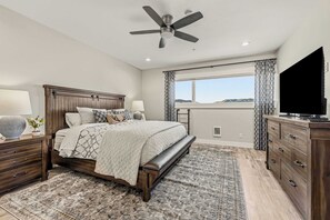 A bedroom with a bed, bedside tables, a TV, a ceiling fan, and a window with curtains.