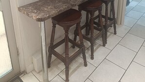 A kitchen with wooden cabinets, a granite countertop, and three wooden stools.