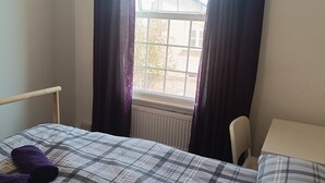 A bedroom with a bed, a chair, a window with curtains, and a radiator.
