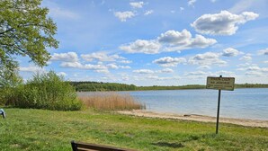 A bench in a grassy area with a lake and a sign in the background. - Comfortable House With a Sauna, Close to the Lake (Purda)