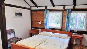 A bedroom with a wooden bed, two bedside tables, a chair, a window with curtains, and a framed picture on the wall. - Comfortable House With a Sauna, Close to the Lake (Purda)