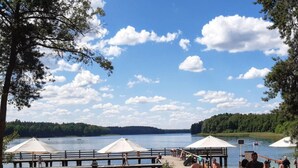 A lakeside beach with a pier, umbrellas, and people relaxing. - Comfortable House With a Sauna, Close to the Lake (Purda)