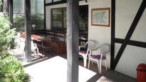 A covered outdoor area with a wooden table and chairs, a bench, and a white trash bin. - Comfortable House With a Sauna, Close to the Lake (Purda)