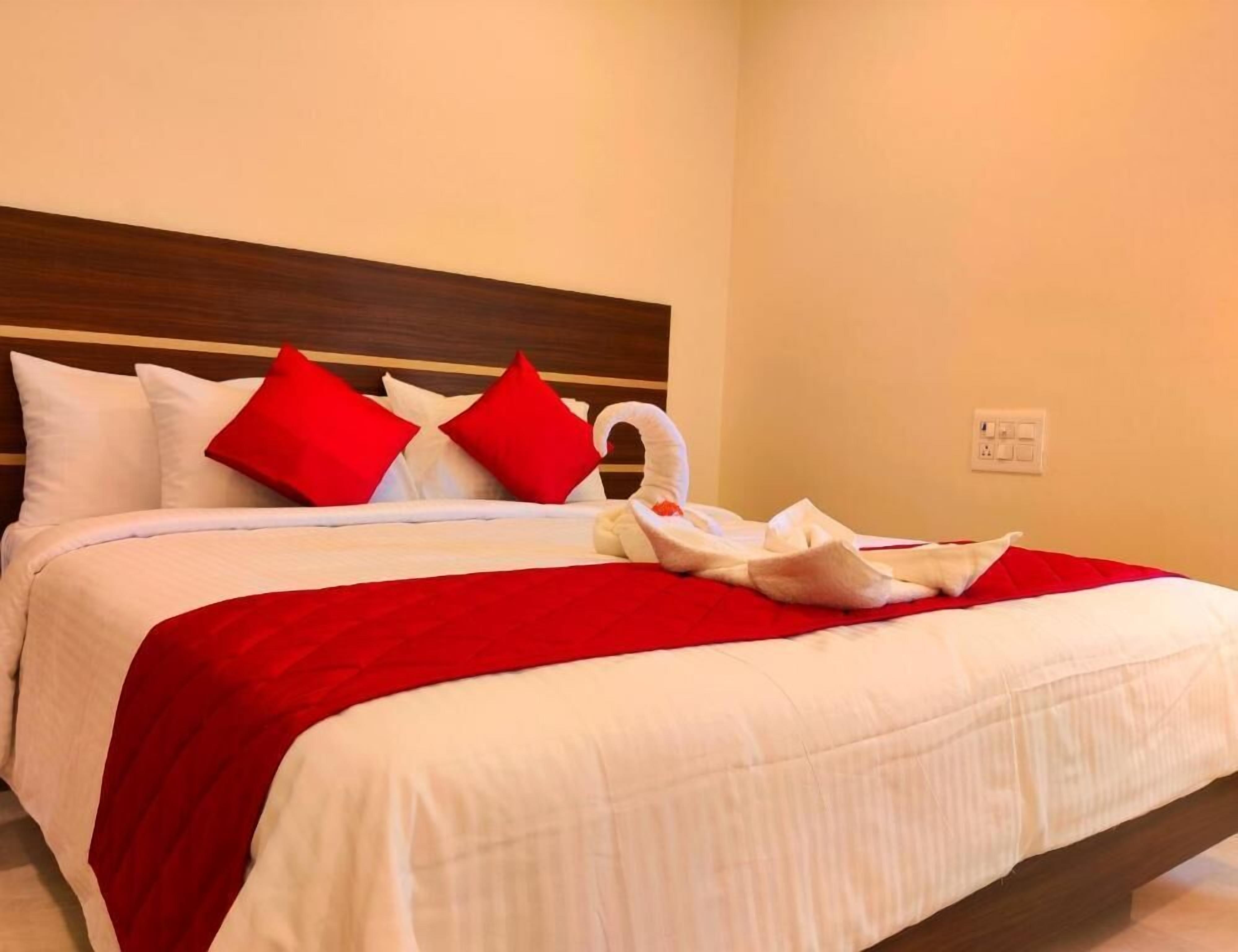 Una cama bien tendida con ropa blanca y almohadas rojas, una toalla blanca y un cabecero de madera.