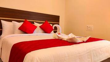 Una cama bien tendida con ropa blanca y almohadas rojas, una toalla blanca y un cabecero de madera.