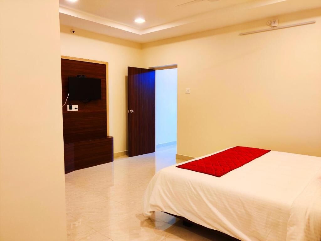 Un dormitorio con cama, televisor montado en la pared y una puerta que da a otra habitación.