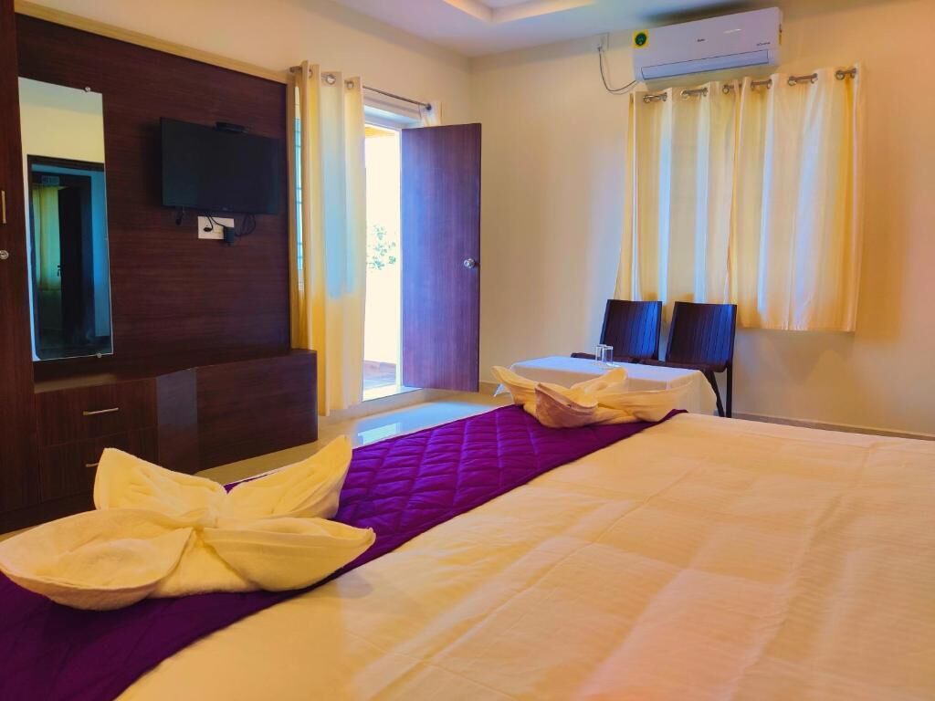 A hotel room with a bed, a TV, a desk, and a window with curtains.
