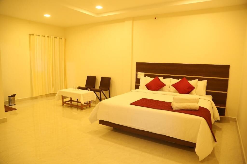 Una habitación de hotel con una cama grande, una mesita pequeña, dos sillas y una cortina.