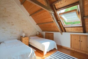 Une chambre avec un plafond en pente, un puits de lumière, un lit, une table de chevet, une armoire et un tapis à rayures.