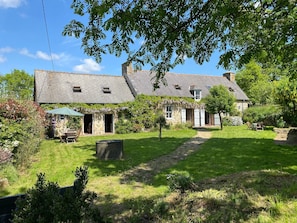 Une maison en pierre avec une cour verdoyante, un patio couvert et un puits en pierre.