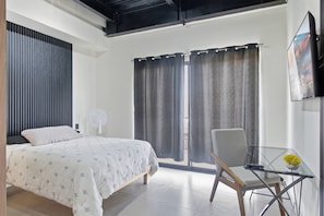 A modern bedroom with a bed, a chair, a glass table, and a window with curtains. - Industrial Loft | 2 Queen Beds & Terrace (Durango)