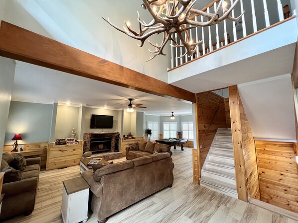 A spacious living room with a fireplace, a pool table, and a staircase leading to an upper level.