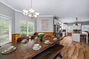 A modern kitchen with a central island, wooden dining table, and a chandelier.