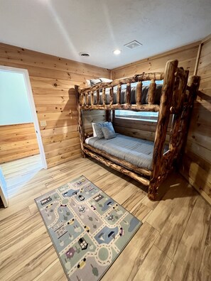 Een houten kamer met een stapelbed, een vloerkleed met dessin en een raam.