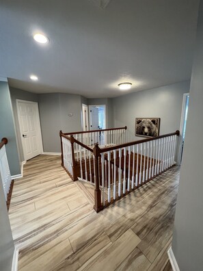 A spacious hallway with a wooden staircase, a white door, and a framed picture on the wall.