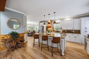 A modern kitchen with a central island, bar stools, white cabinetry, and a wooden accent wall. - Gatlinburg, Sleeps 21, Hot Tub, Mt. Le Conte Views, Pool Table, Theater Room (Gatlinburg)
