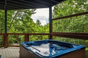 Een hottub op een houten terras, met uitzicht op weelderige groene bomen.