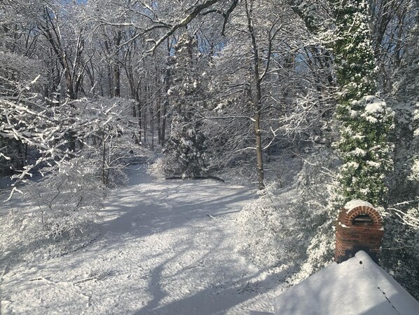 A snow-covered path leading through a forest with a brick structure on the right.