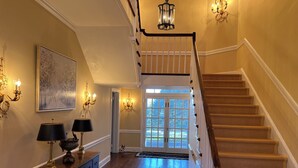A grand staircase with a wooden handrail, a chandelier, and a large window at the top. - Fabulous 4-bedroom villa in tranquil Caves Valley area in Baltimore County MD (Owings Mills)