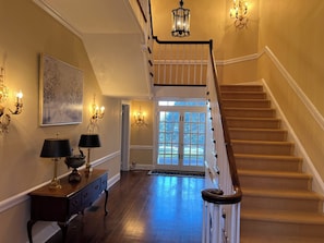A grand staircase with a wooden handrail, a chandelier, and a large window at the top.