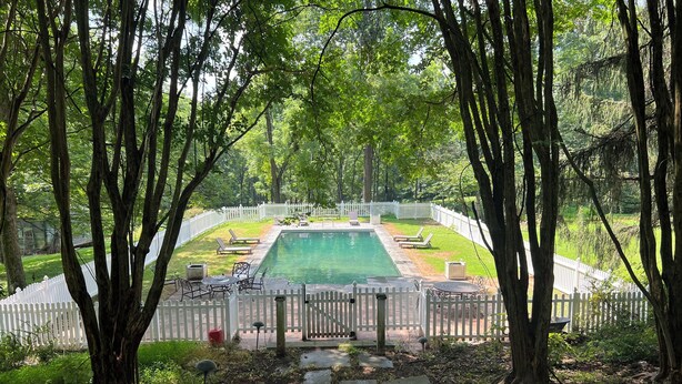 A rectangular swimming pool with a white fence, surrounded by trees and a white picket fence. - Fabulous 4-bedroom villa in tranquil Caves Valley area in Baltimore County MD (Owings Mills)