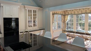 A kitchen with white cabinetry, a black countertop, and a window with floral curtains. - Fabulous 4-bedroom villa in tranquil Caves Valley area in Baltimore County MD (Owings Mills)