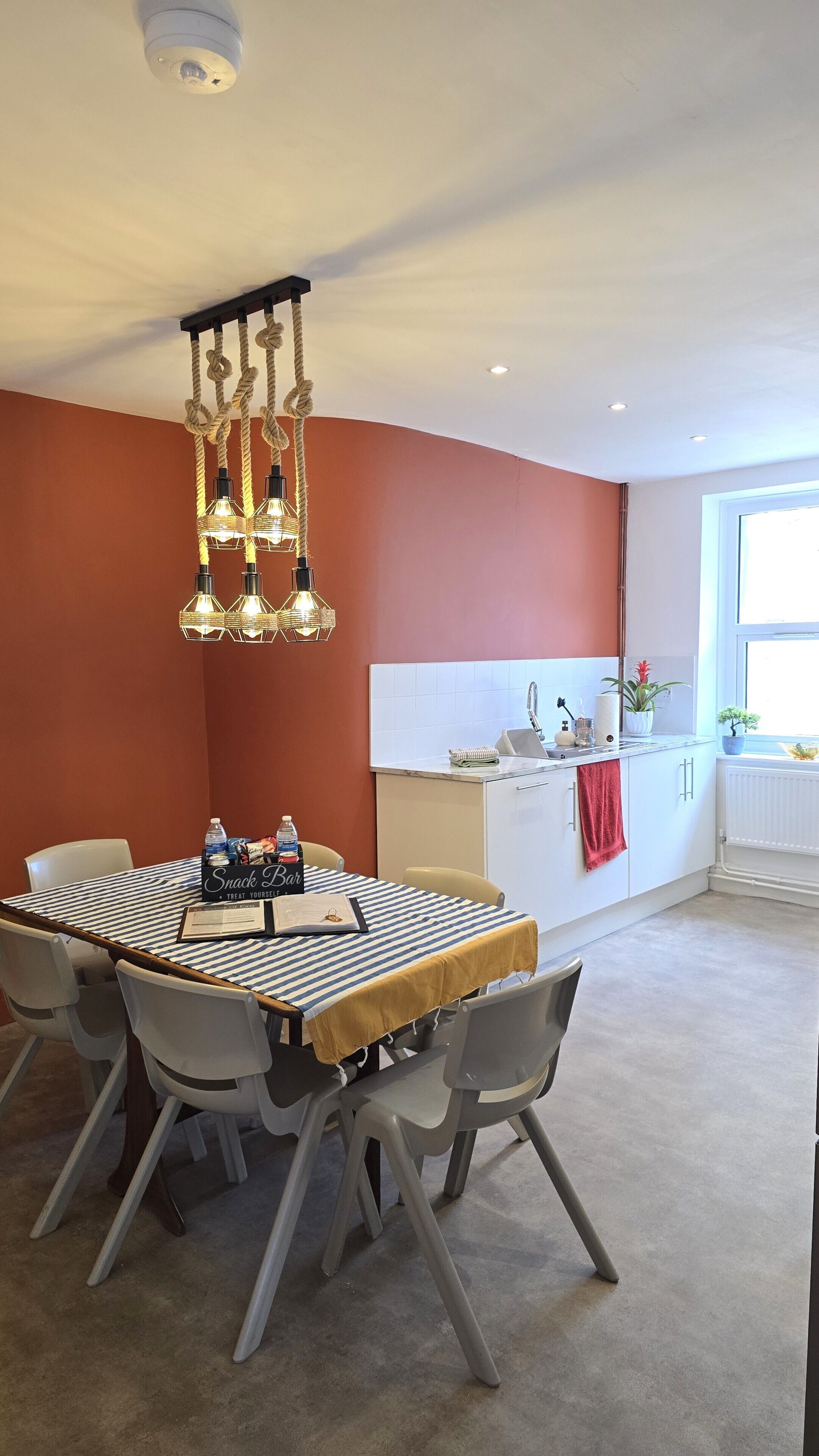 A dining area with a round table, chairs, a chandelier, and a kitchen in the background.