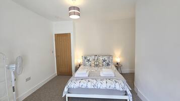 A bedroom with a bed, bedside lamps, a ceiling fan, a wooden door, and a light fixture.