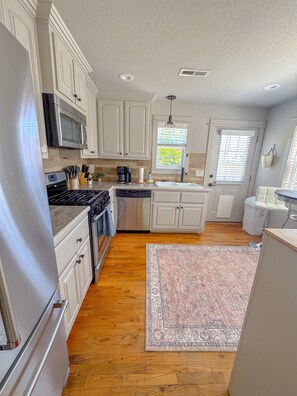 A kitchen with white cabinets, a stainless steel refrigerator, a microwave, a dishwasher, and a coffee maker. - The Pink B • Walk to Square •Airship•Crystal Bridges • MTB Trails (Bentonville)