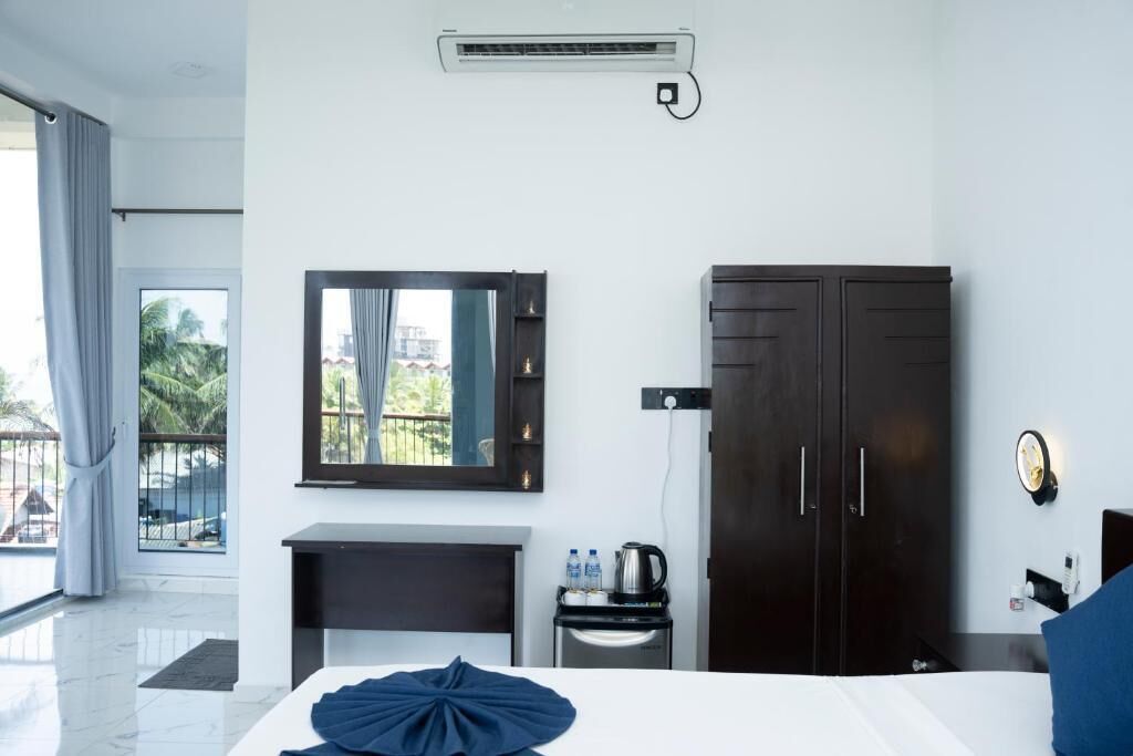 A modern hotel room with a bed, a desk, a wardrobe, a mirror, and a view of the outside.