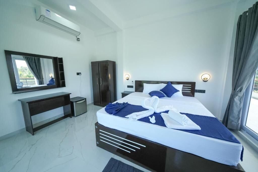 Een moderne hotelkamer met een groot bed, een nachtkastje, een kledingkast, een spiegel en een raam met gordijnen.