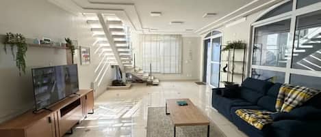 Un salon moderne avec un téléviseur, un canapé, une table basse, un escalier et de grandes fenêtres.