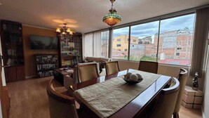Zona pranzo con tavolo, sedie, lampadario, libreria e televisione.
