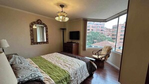 Una camera da letto con un letto, una sedia, una TV e una finestra con vista sugli edifici.