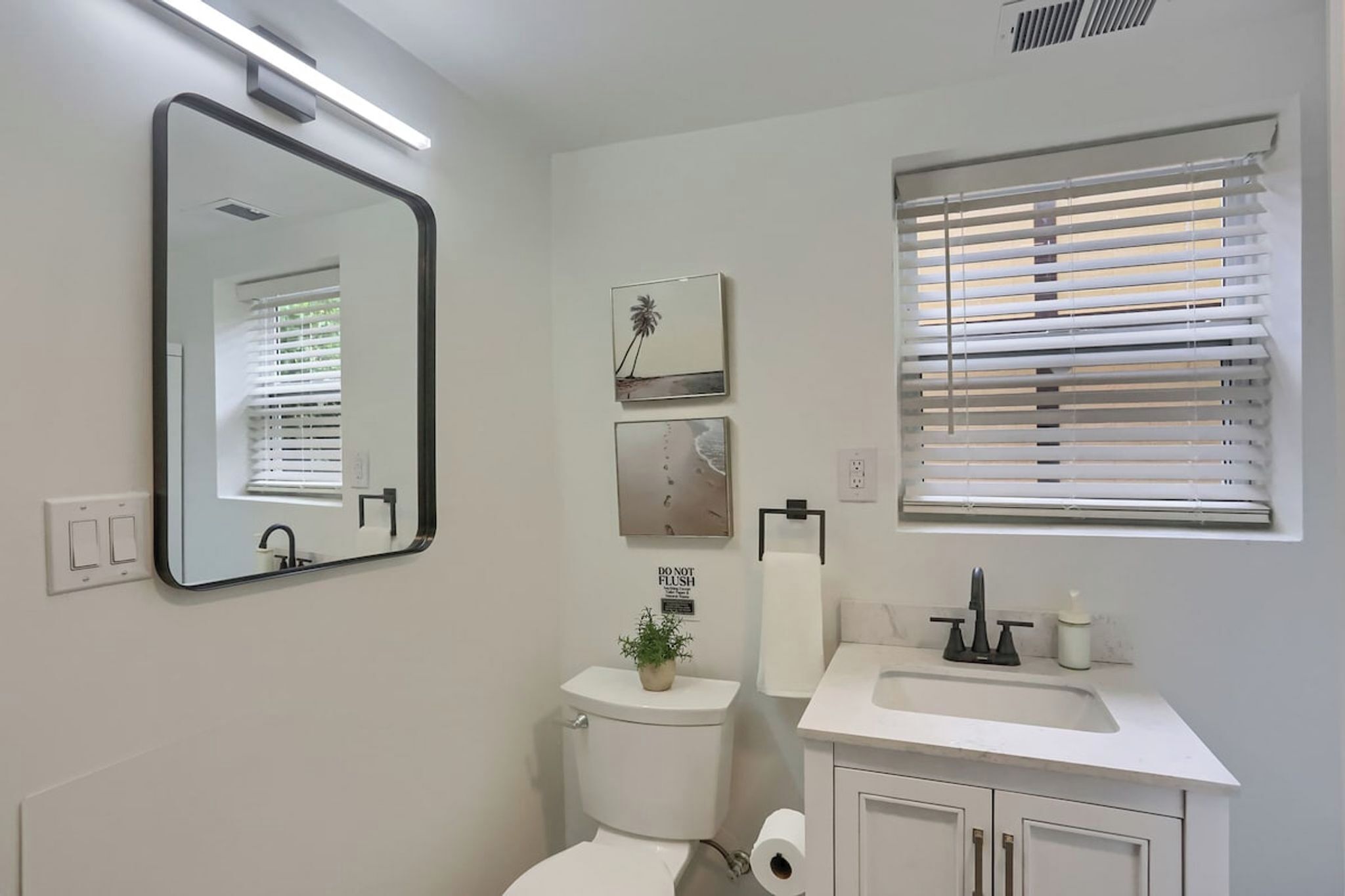 Een moderne badkamer met toilet, wastafel, spiegel en raam met zonwering.