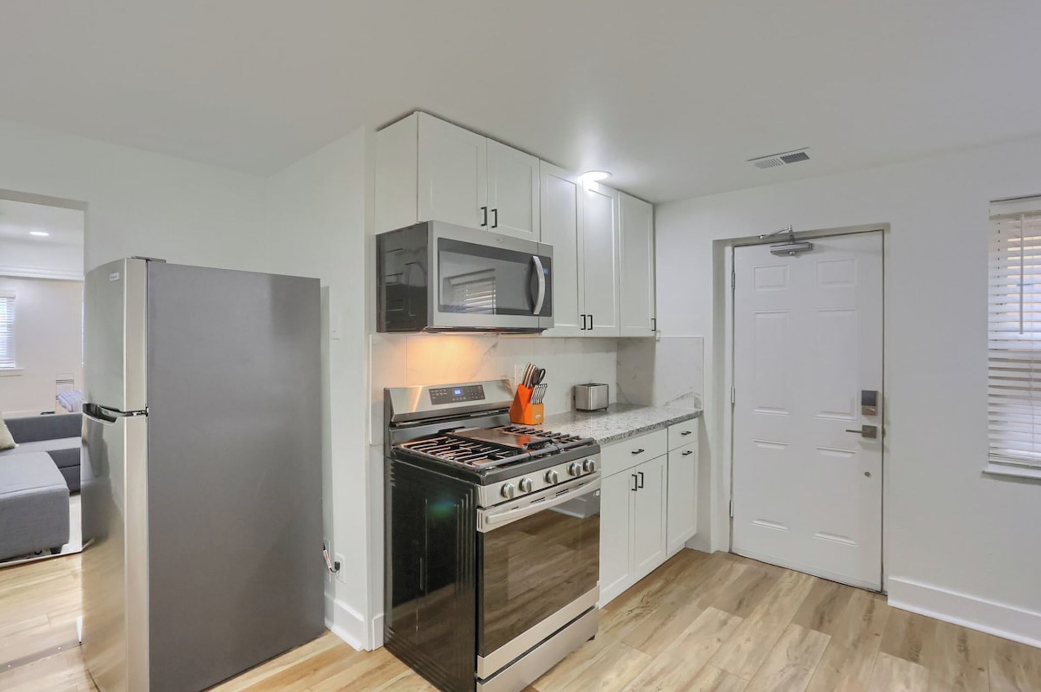 A compact kitchen with a refrigerator, microwave, stove, and white cabinets.