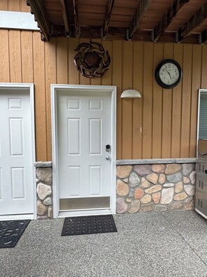 A building entrance with a white door, a stone wall, a clock, and a metal doorbell.