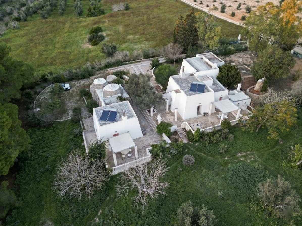 An aerial view of a residential area with multiple white buildings, some with solar panels, surrounded by greenery and trees.