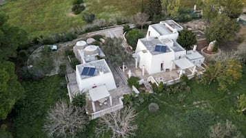 An aerial view of a residential area with multiple white buildings, some with solar panels, surrounded by greenery and trees.