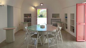 Een eetgedeelte met een ronde tafel en stoelen, een keuken met planken, en een roze deur.