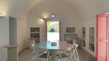 Un coin repas avec une table ronde et des chaises, une cuisine avec des étagères et une porte rose.